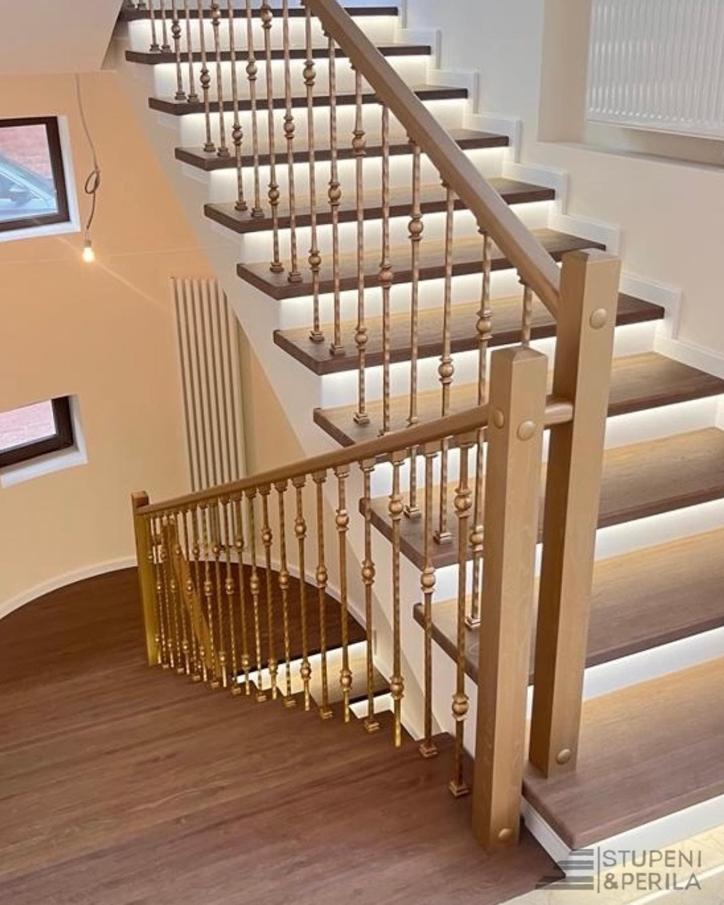 Curved wooden staircase with dark treads, white risers, LED lighting, and ornate gold metal railings.