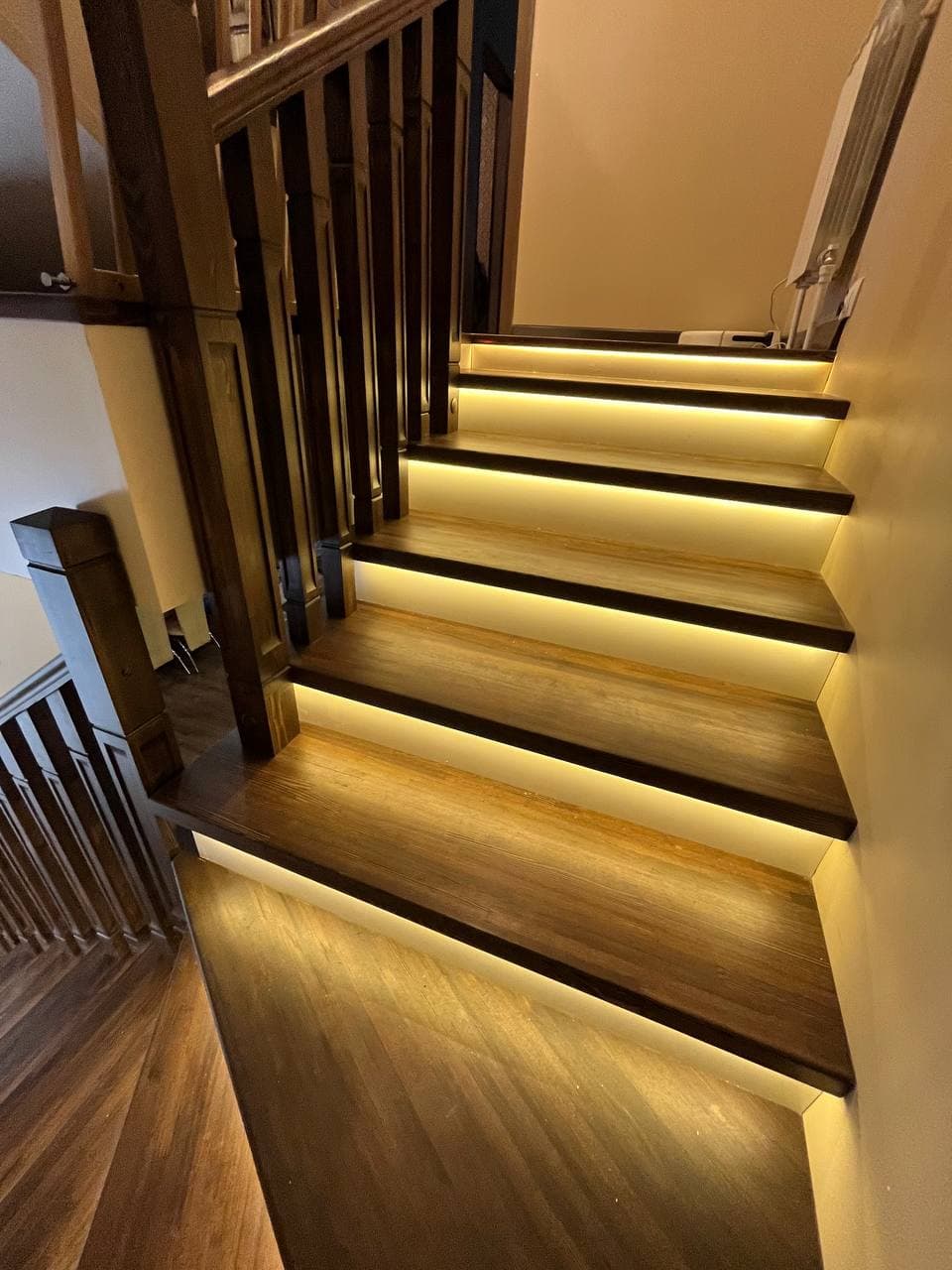 Dark wooden staircase featuring warm LED strip lighting glowing under each step and banister.